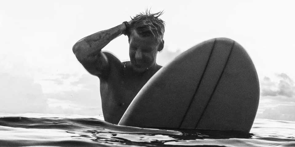 Surfer mit Surfbrett im Meer streicht sich das nasse Haar aus dem Gesicht